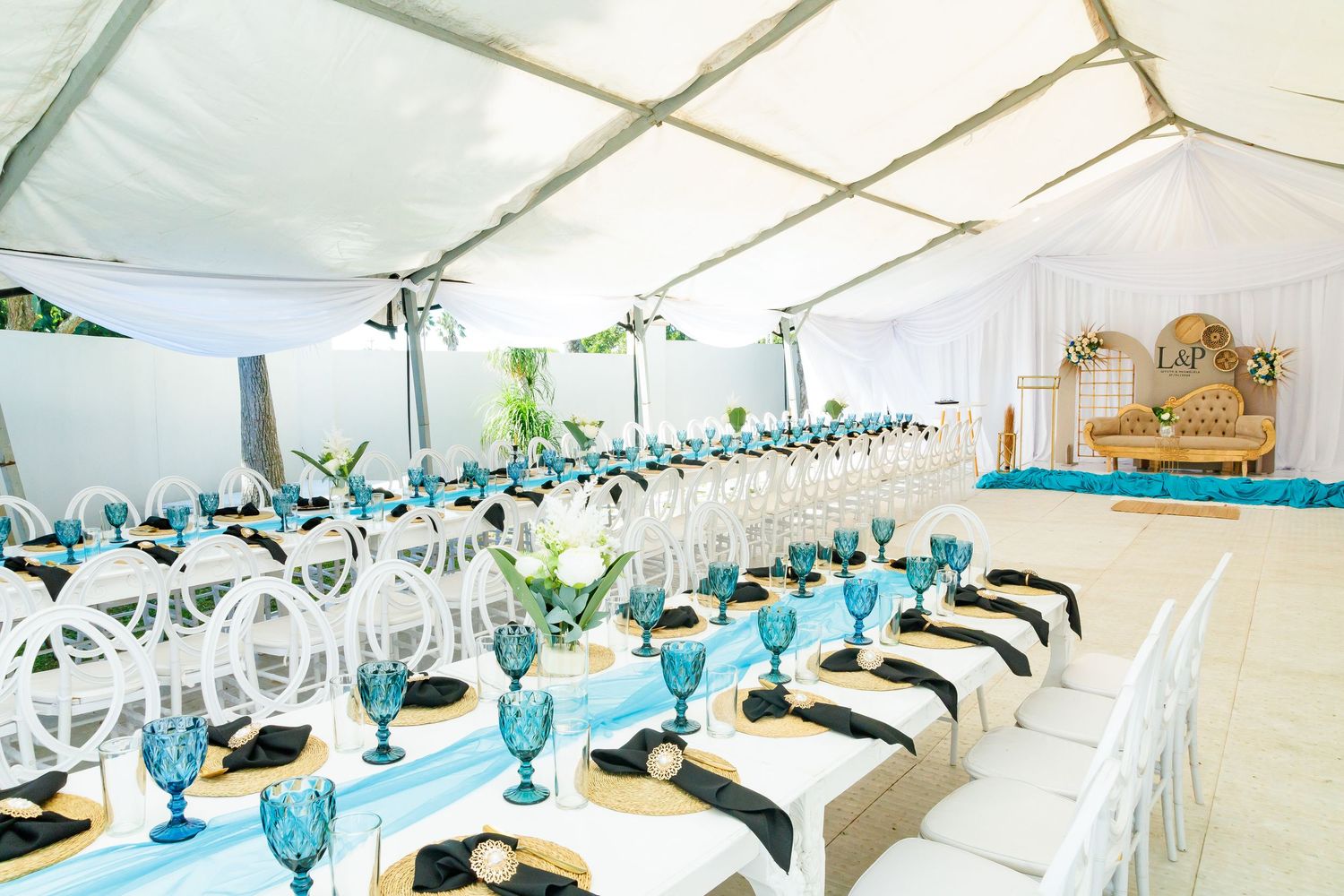 Elegant wedding reception tent with long tables, turquoise glassware, and decorative centerpieces.