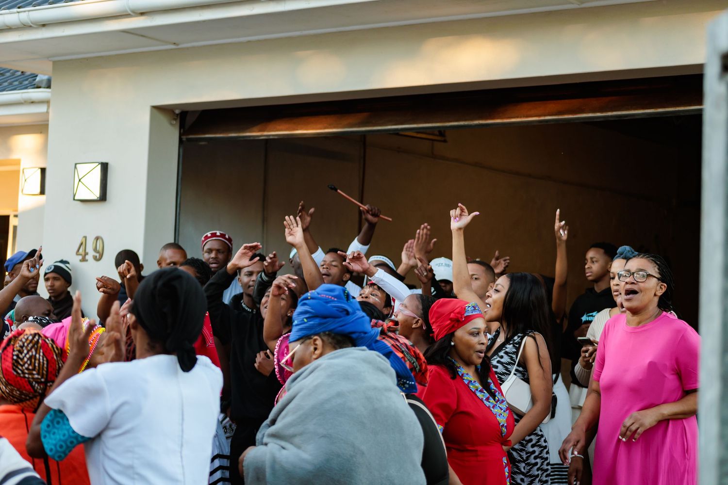 Joyful crowd celebrating with raised hands at entrance of home during African cultural event.