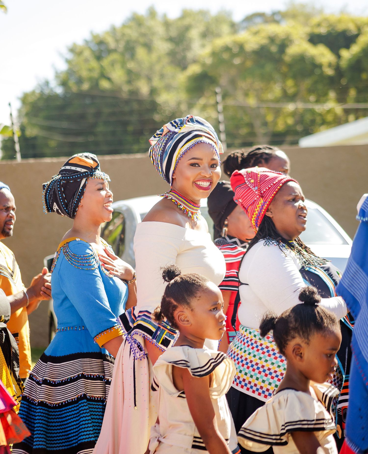 Women in colorful traditional African attire and head wraps gather outdoors at a cultural celebration.