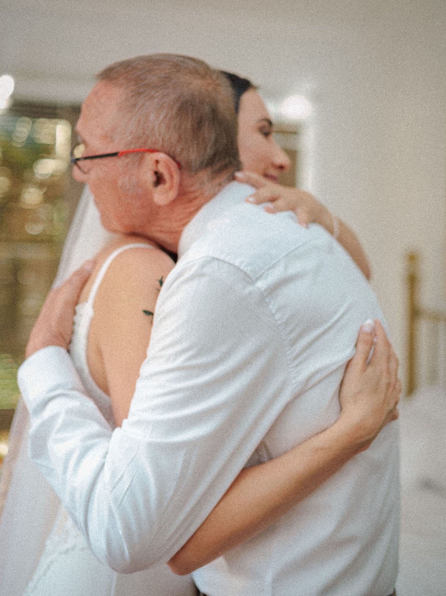 Emotional first look moment as bride in veil embraces older man in white shirt at wedding venue.