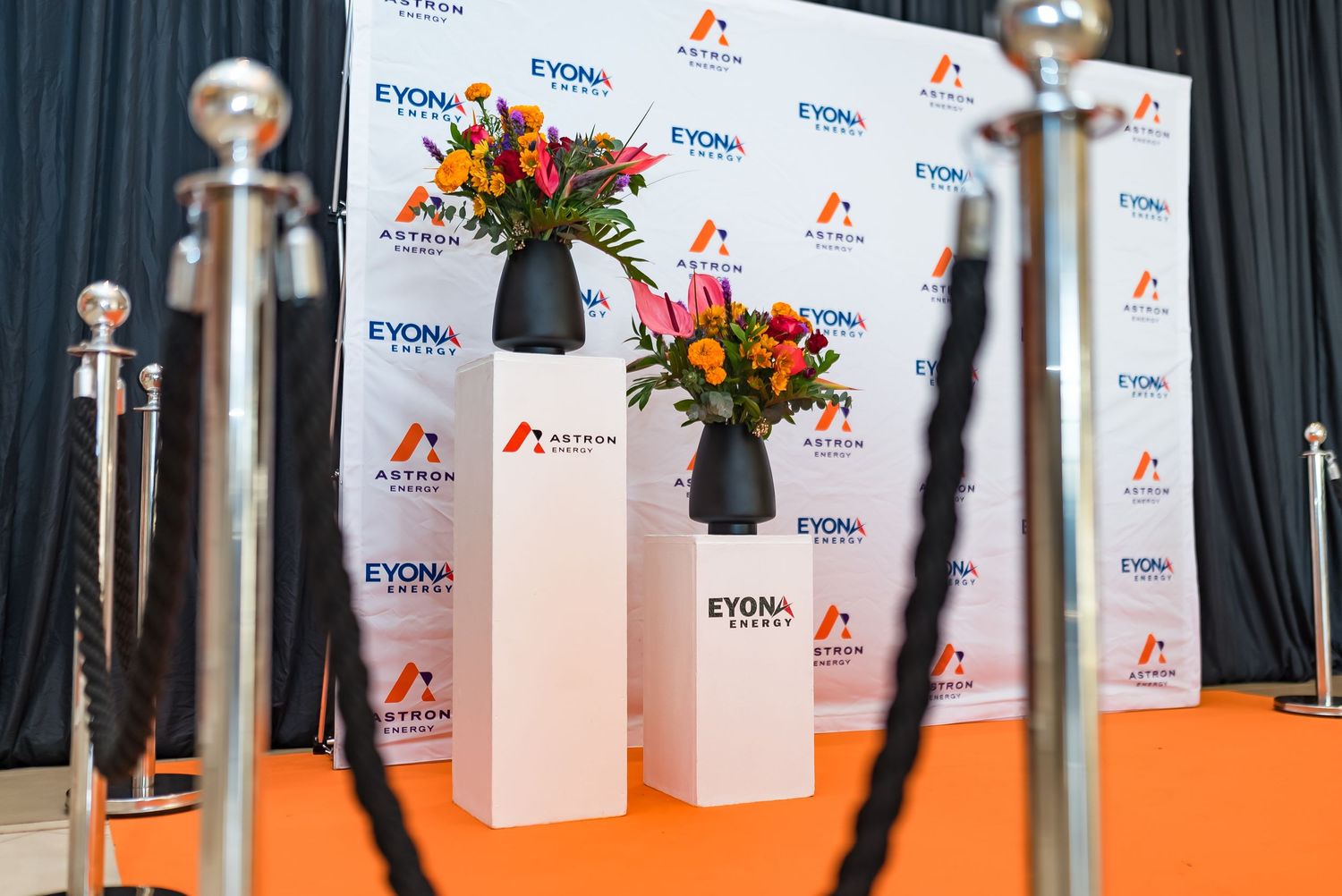 Eyona Energy and Astron Energy branded photo backdrop with floral arrangements on orange carpet.