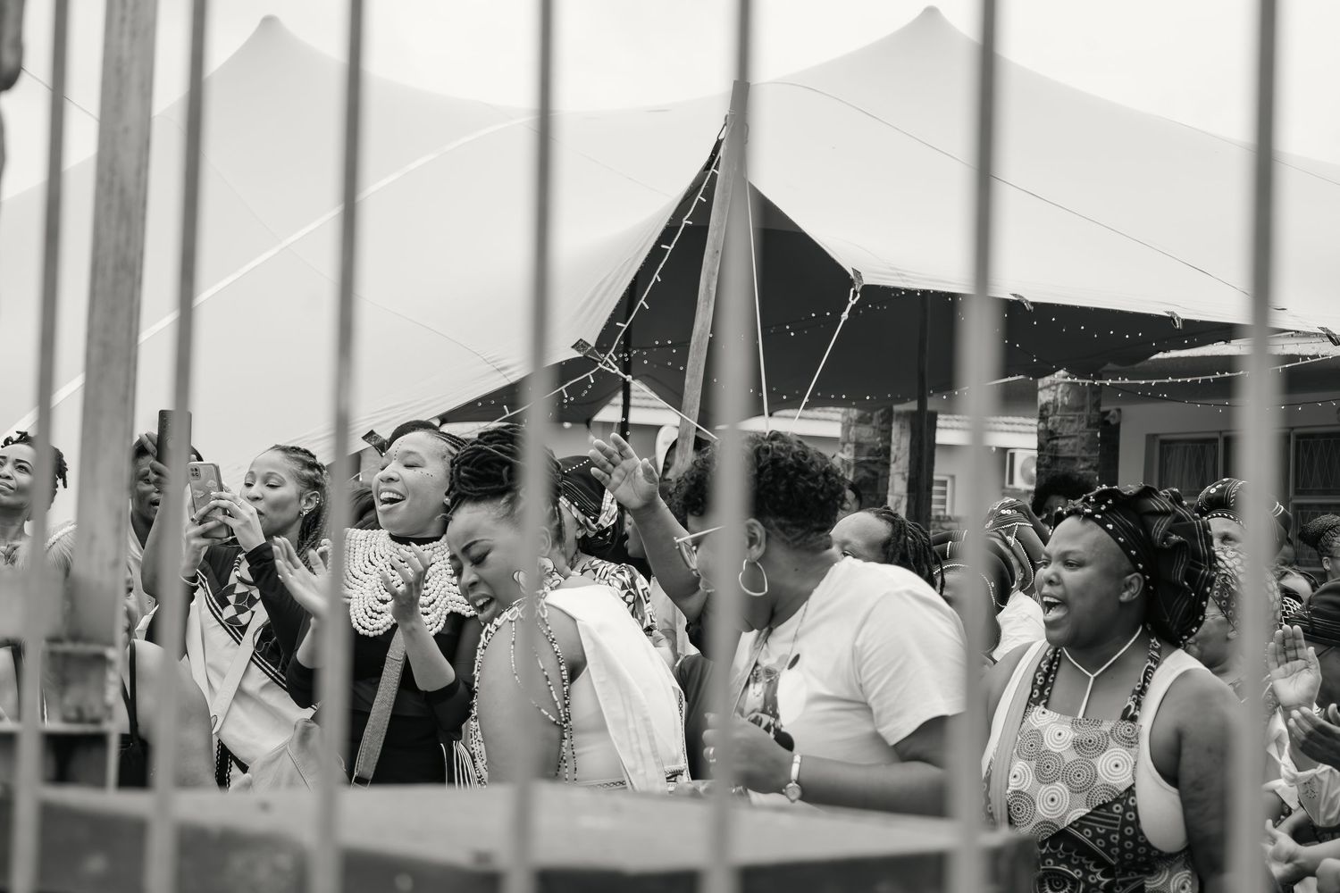 Black and white photo of joyful wedding guests celebrating outdoors near a large white reception tent.