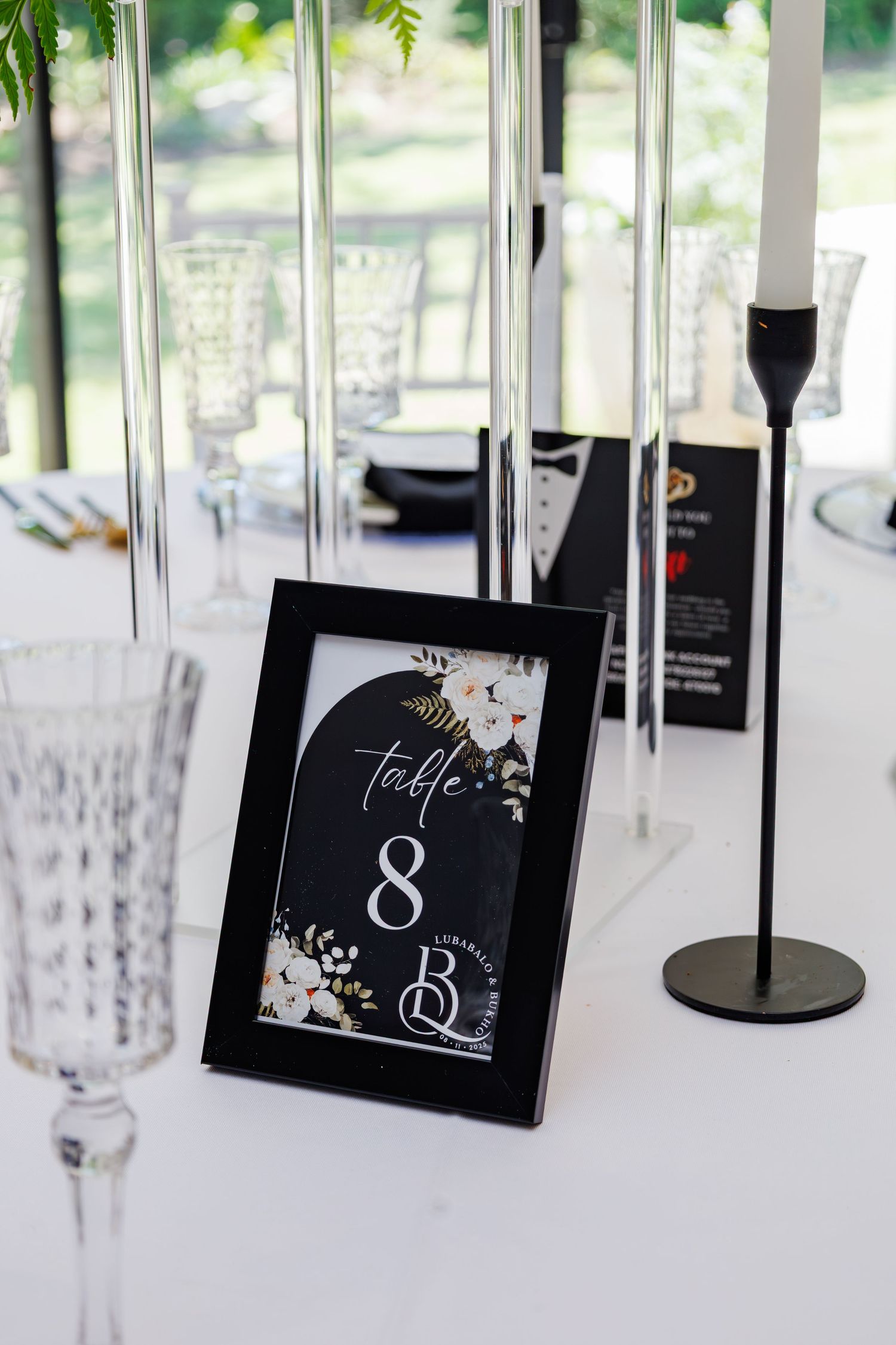 Black framed Table 8 sign with floral design displayed on a white wedding reception table setting.