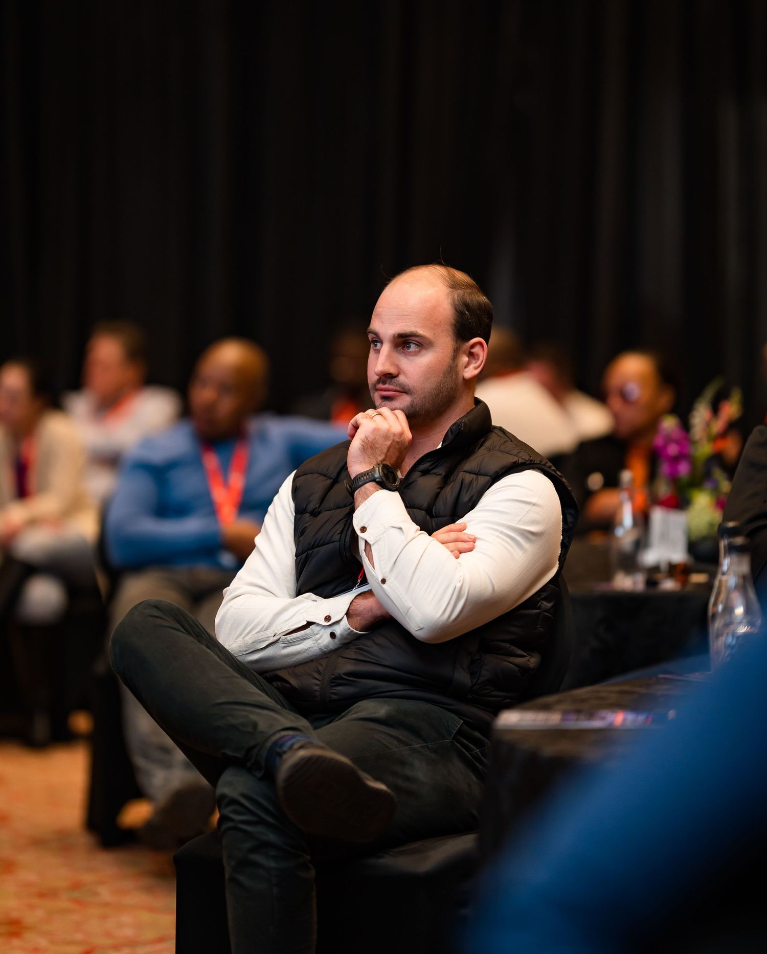 Thoughtful young man with arms crossed listens attentively at a business conference.