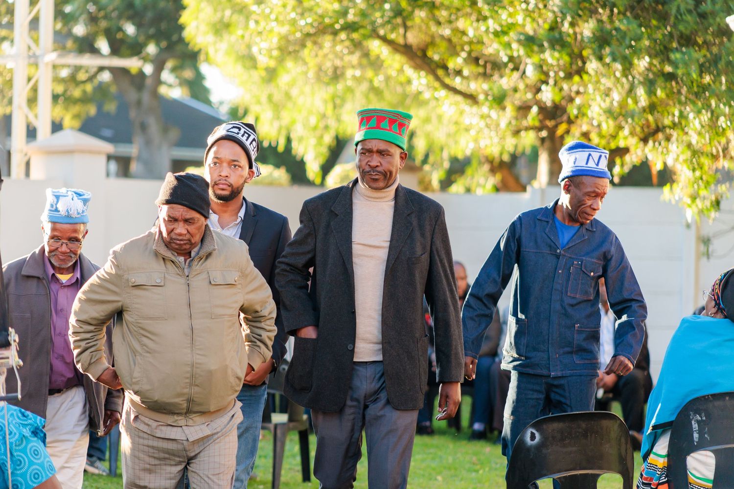 Group of men in traditional Xhosa caps walking together at an outdoor cultural celebration.