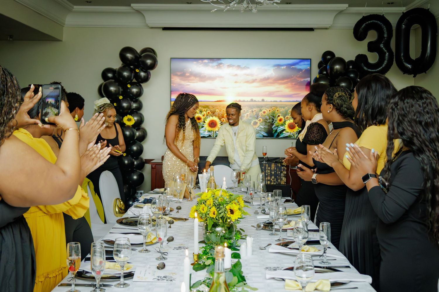 Couple walking between applauding guests at a sunflower-themed 30th birthday dinner celebration.