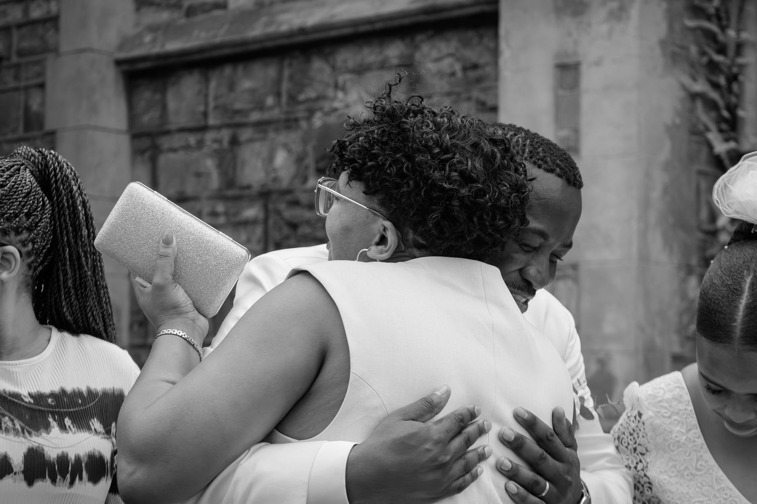 Emotional black and white photo of two people sharing a heartfelt hug at an outdoor wedding celebration.