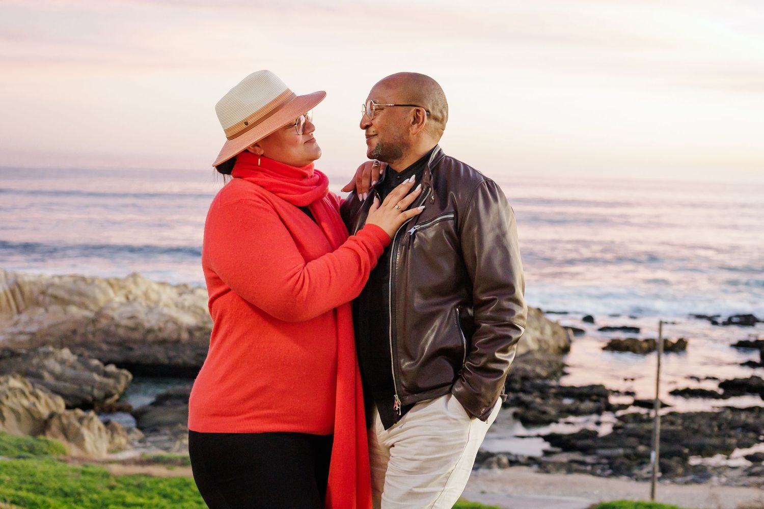 Romantic couple sharing a tender moment on a scenic coastal lawn during a vibrant sunset by the sea.