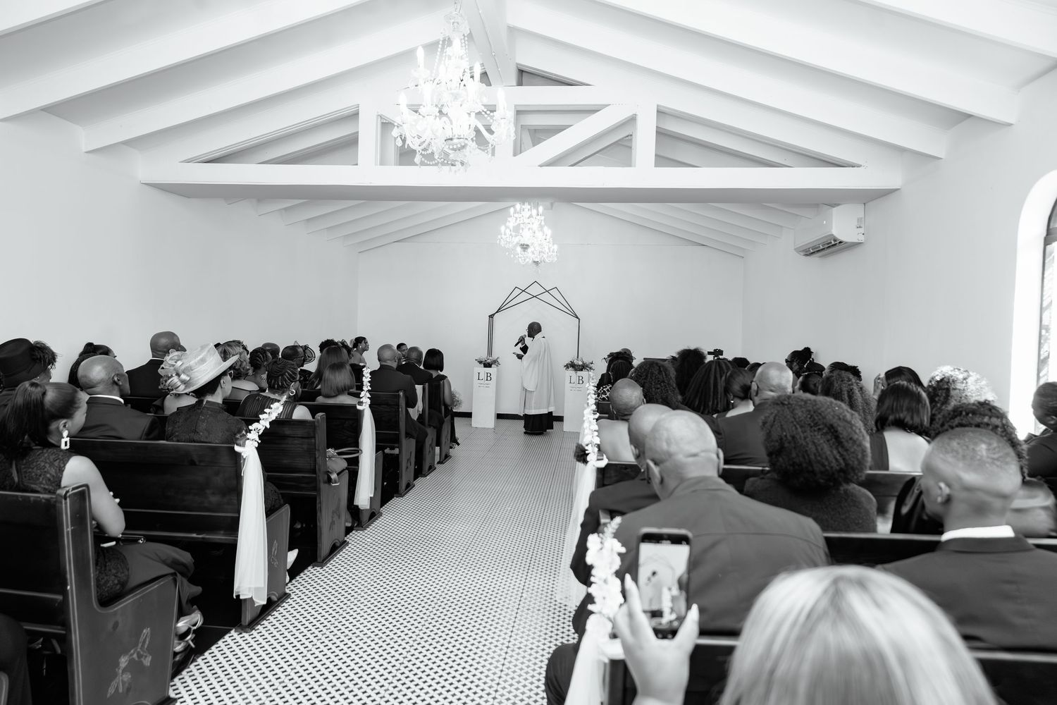 Black and white wide-angle view of wedding ceremony with guests filling chapel pews.
