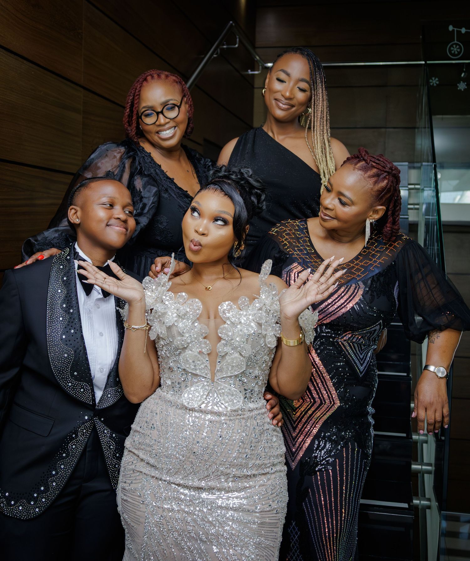 Bride in silver sequin gown posing with four friends in formal attire at elegant venue.