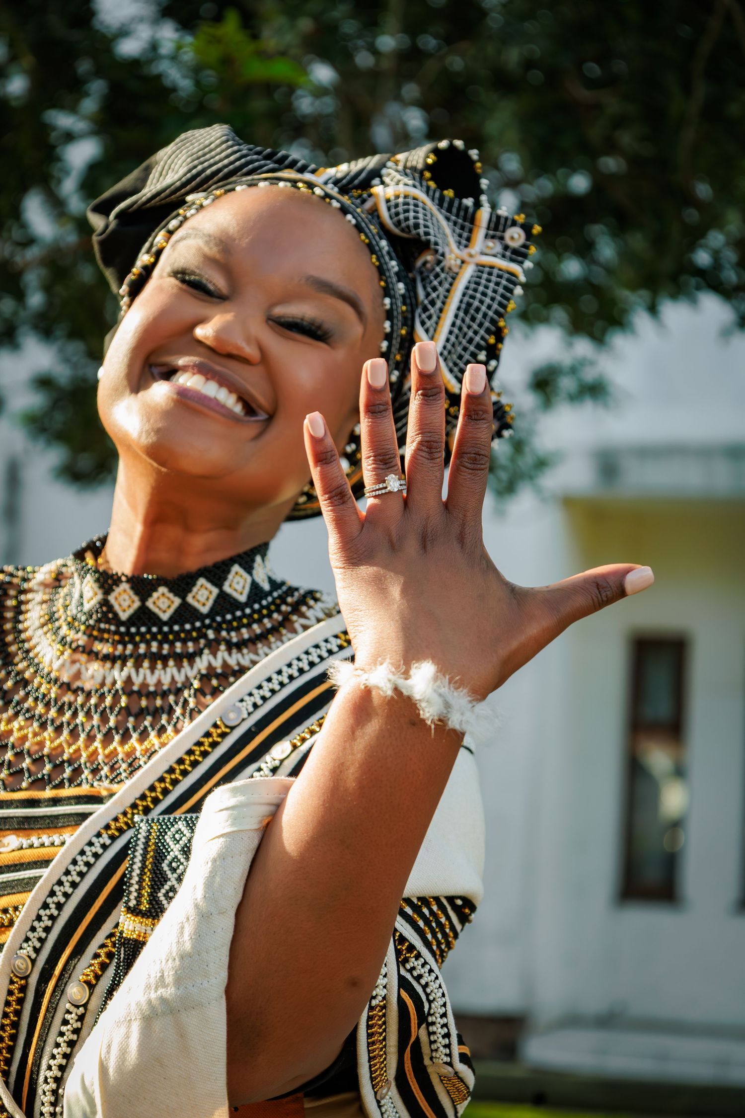 Joyful woman in traditional Xhosa beaded necklace and headwrap proudly displaying her engagement ring.
