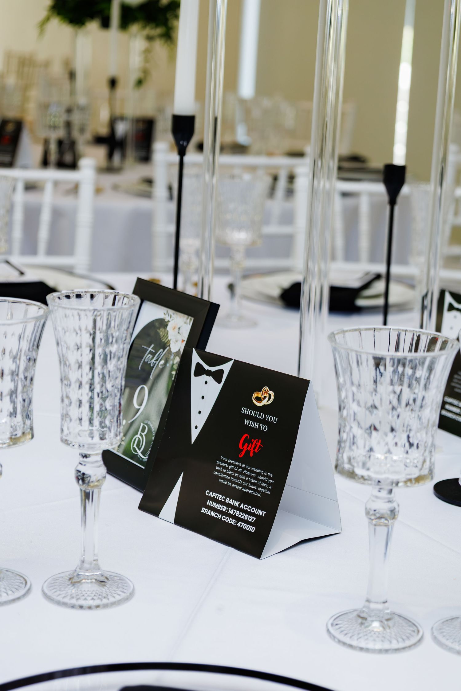 Black and white wedding table setting with crystal glasses, gift card display, and tall candle holders.