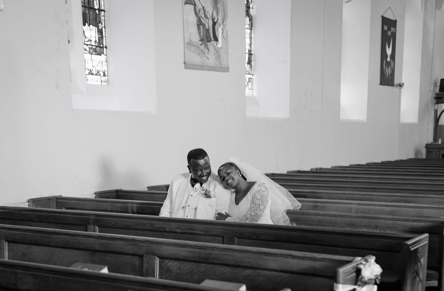 Black and white photo of a bride and groom sharing a tender moment together in a church pew.