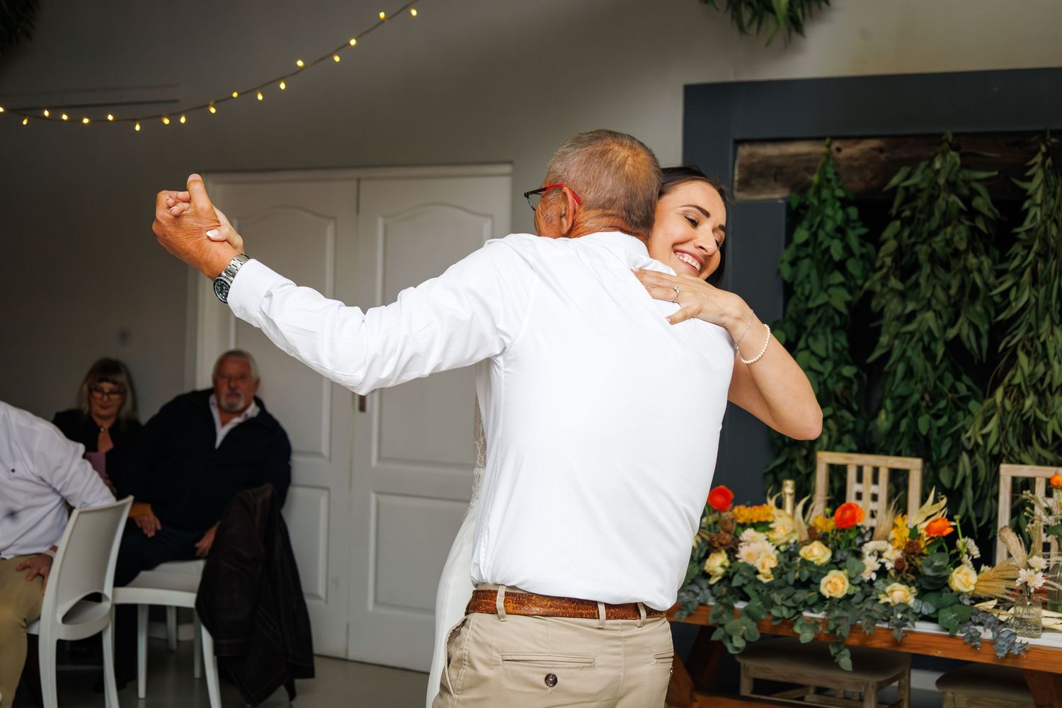 Woman in white dress shares a joyful dance with older man at an elegant wedding reception.
