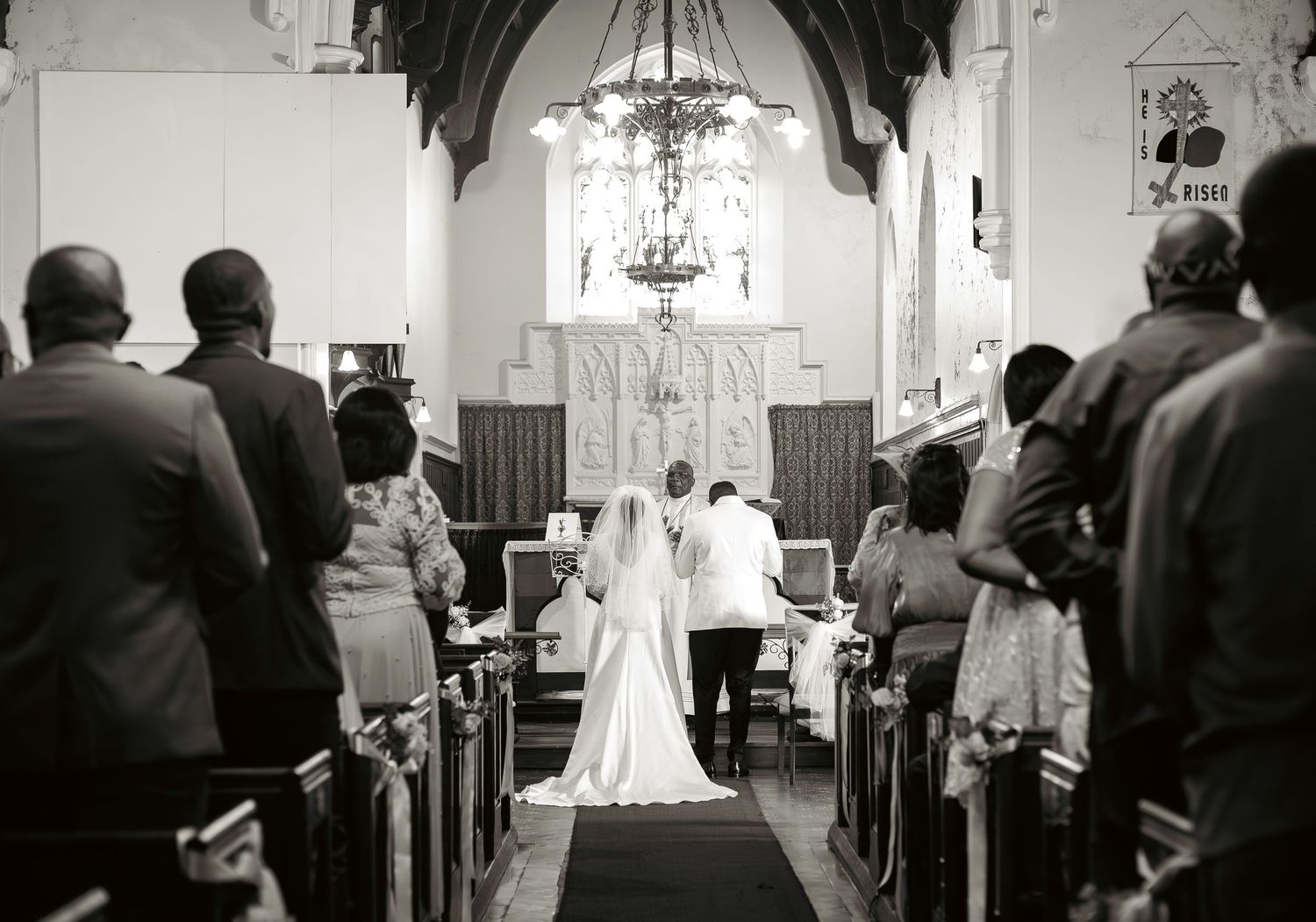 Black and white photo of bride and groom at church altar surrounded by wedding guests.
