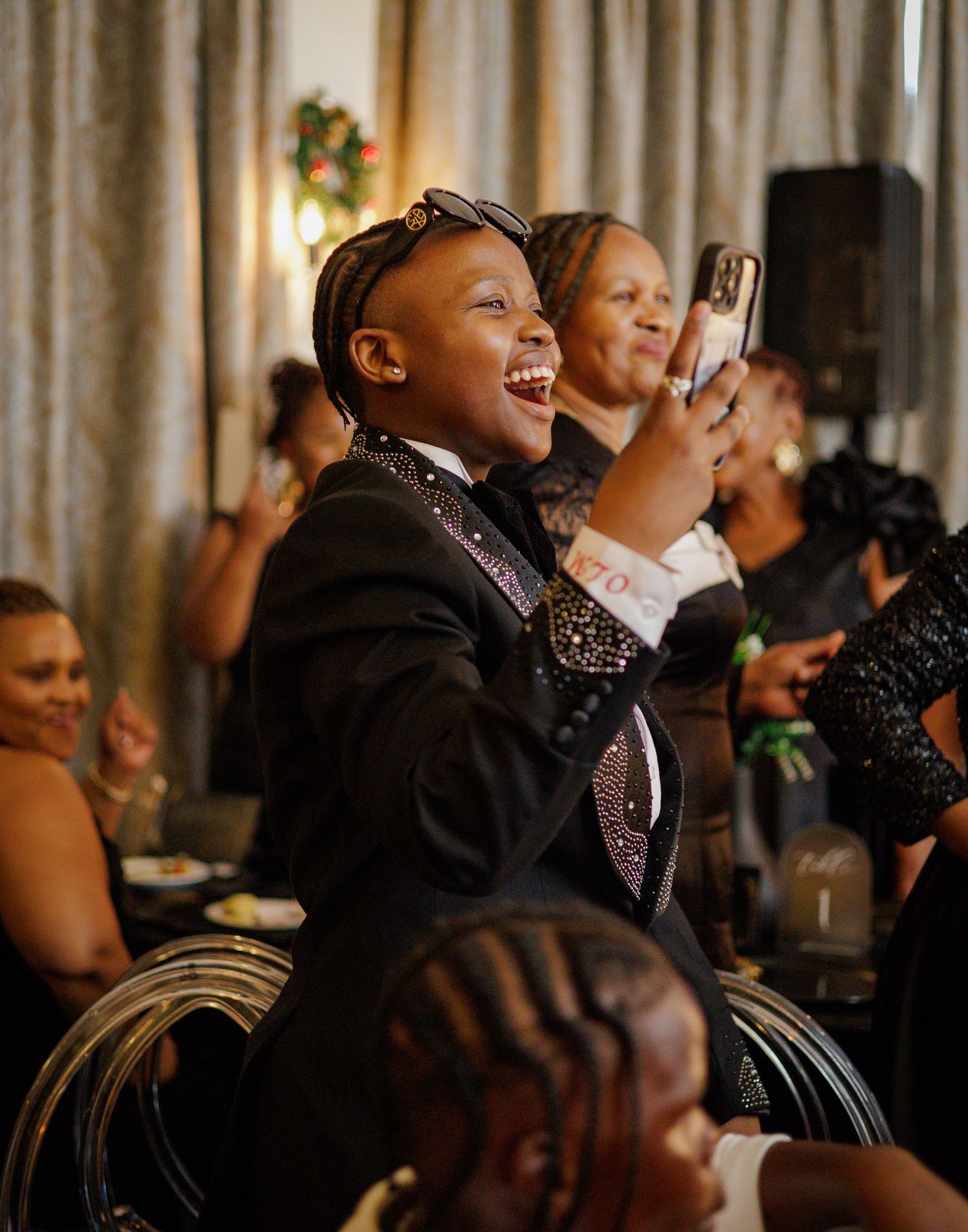 Joyful child in black tuxedo laughs and claps at a festive birthday celebration event.