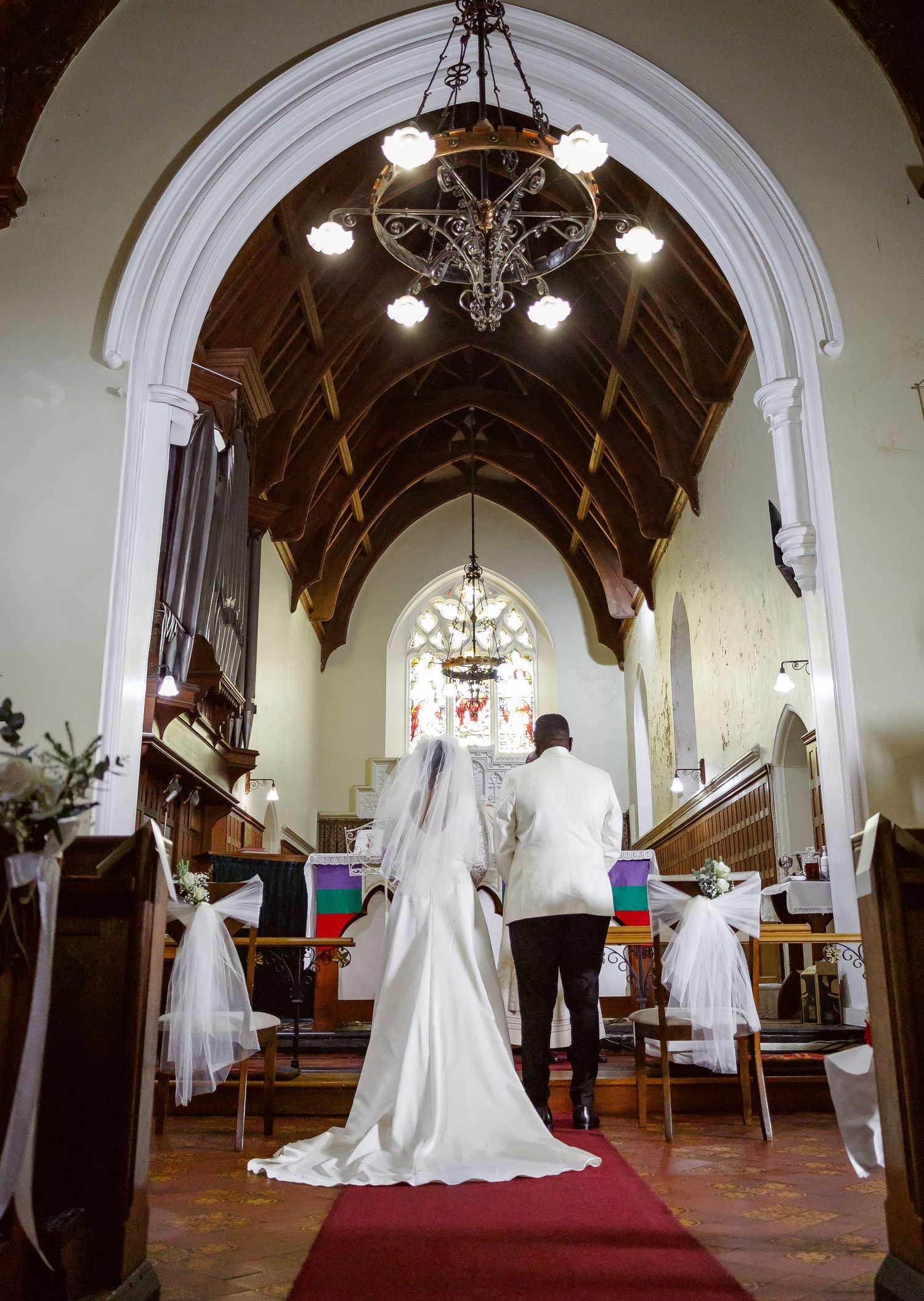 Bride and groom walk down red carpet aisle of decorated church during wedding.