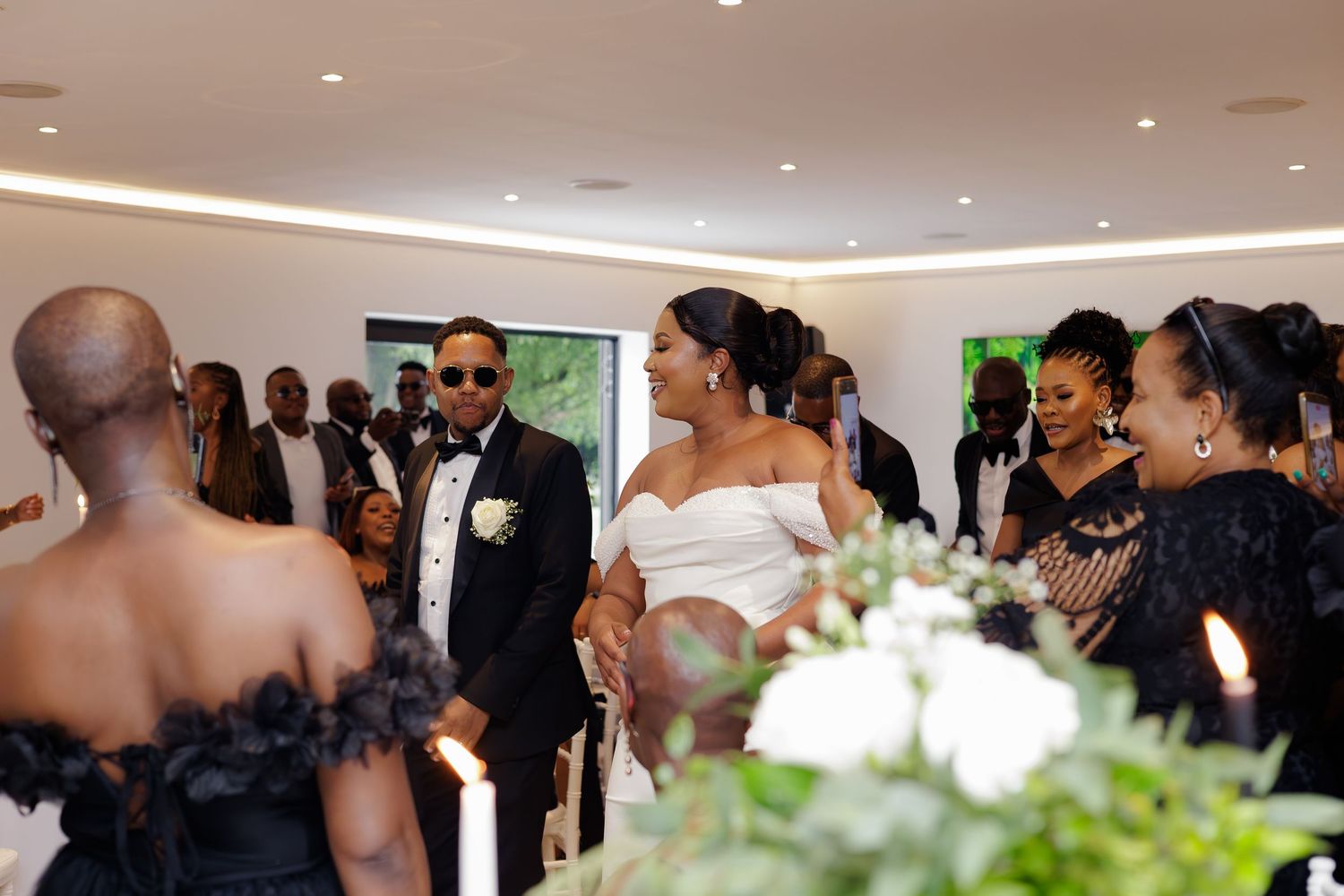 Bride in white off-shoulder gown and groom in black tuxedo sharing a moment during wedding ceremony.