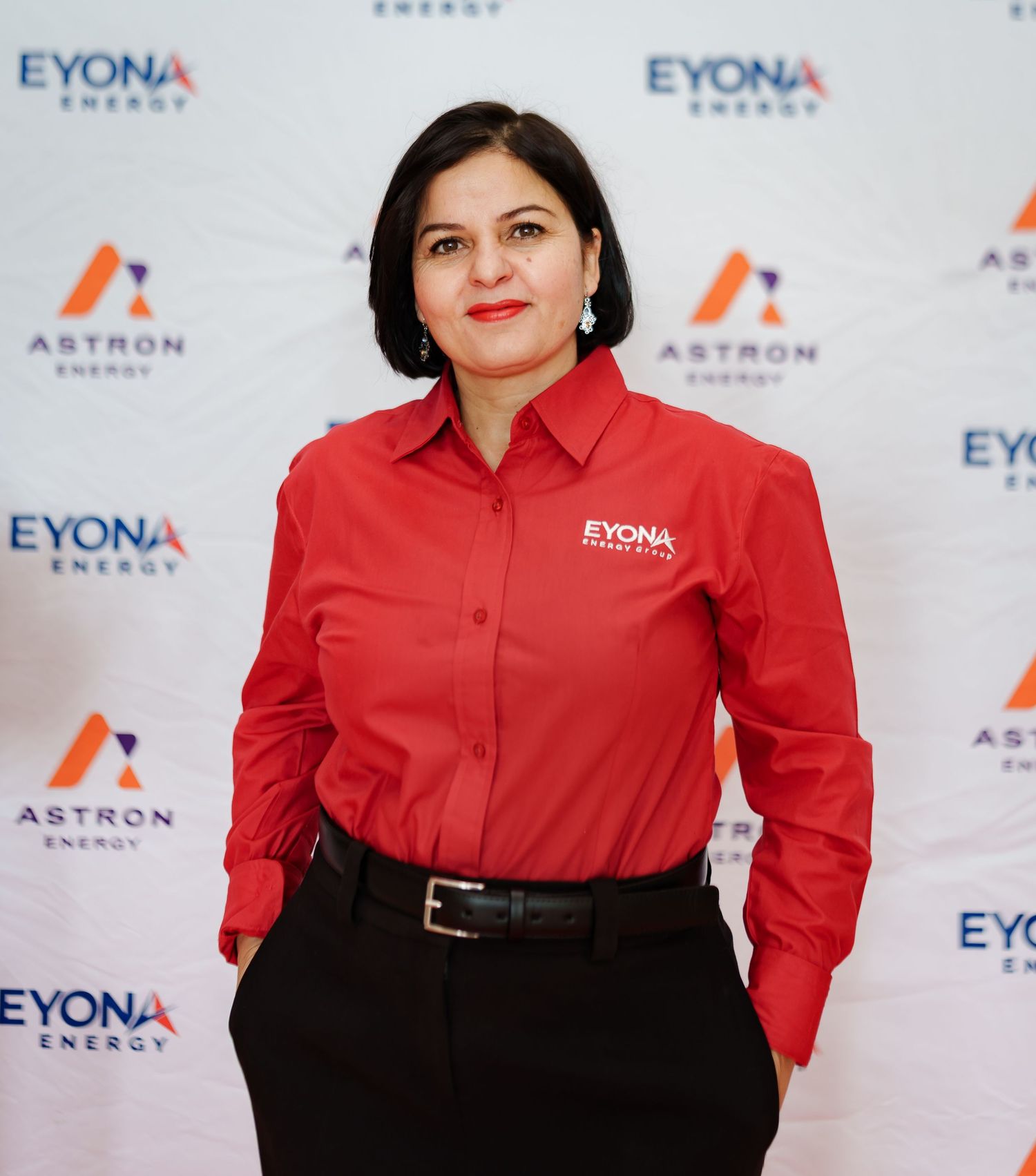 Woman in red Eyona Energy uniform poses before Astron Energy and Eyona Energy branded backdrop.