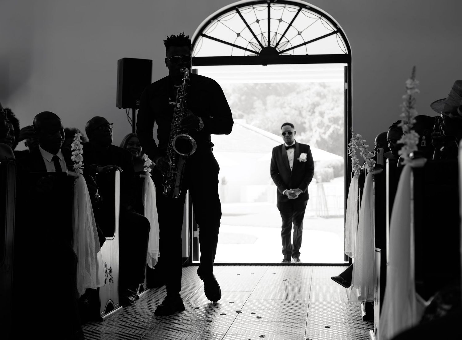 Black and white silhouette of saxophonist performing as groom waits at church entrance.