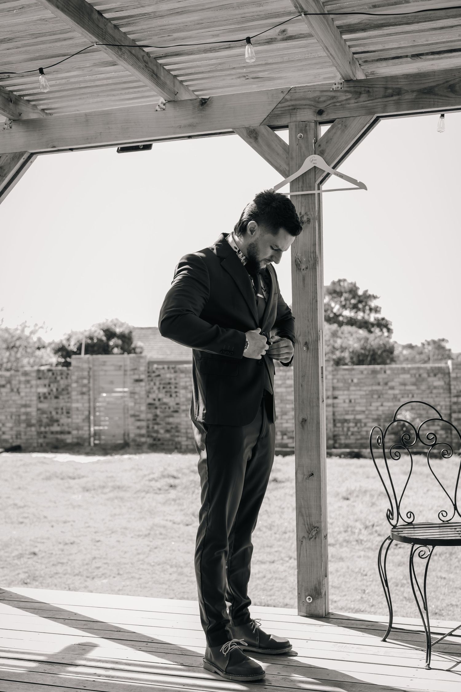 Groom in black suit buttoning jacket in black and white outdoor wedding photo.