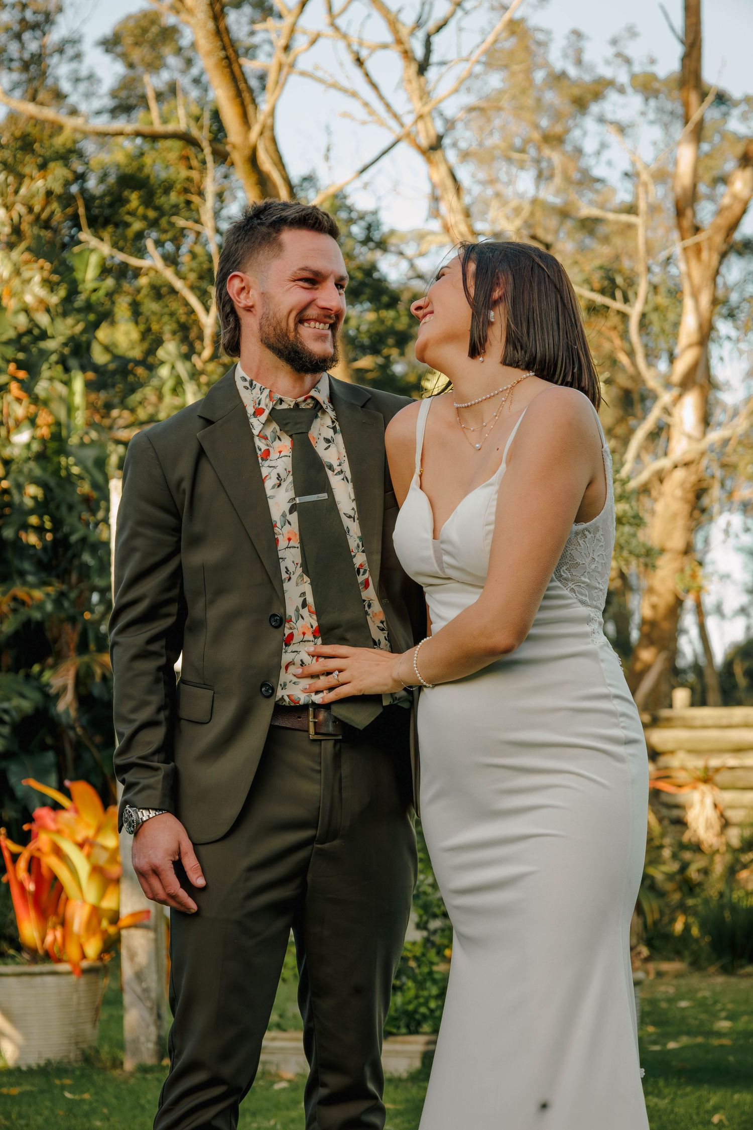 Laughing bride and groom share joyful moment together in sunlit garden wedding portrait.