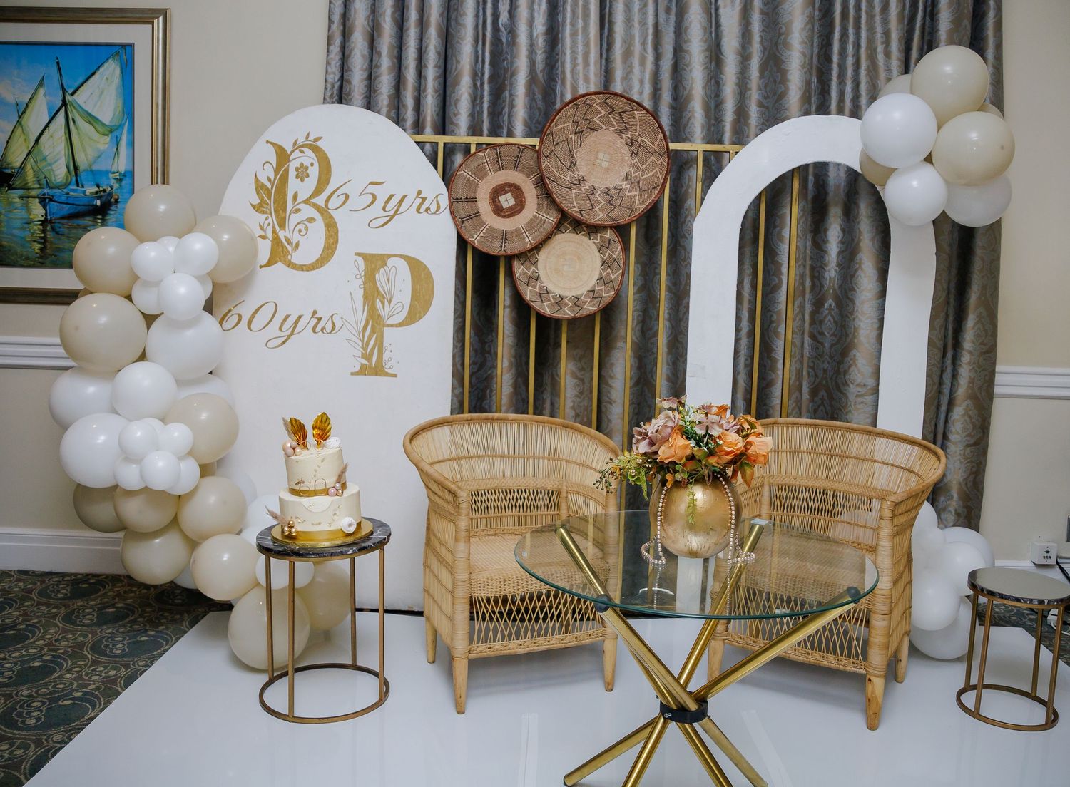 Elegant party backdrop with gold and white balloons, rattan chairs, and anniversary decor.