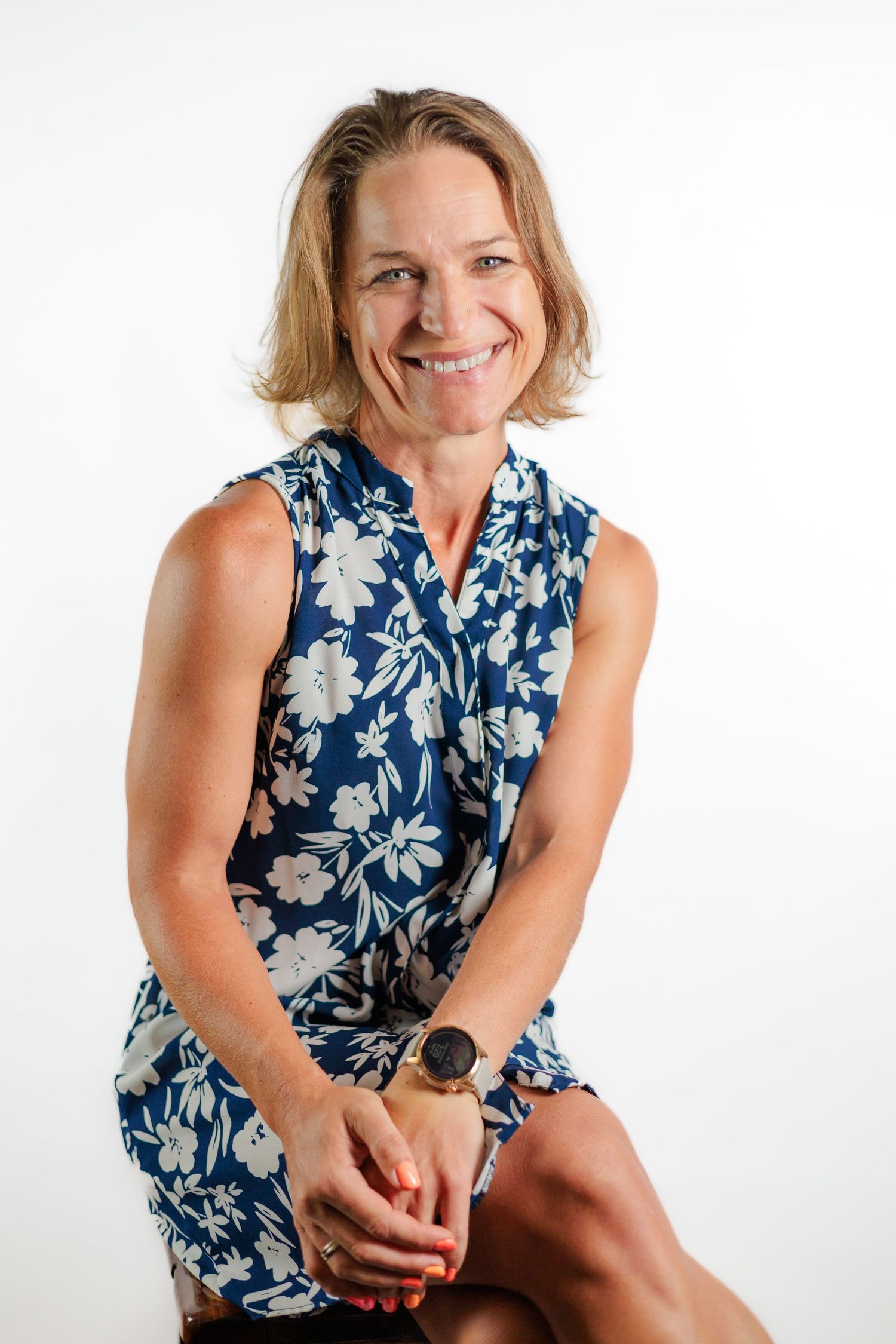 Happy woman in blue floral dress sits smiling in bright studio portrait.