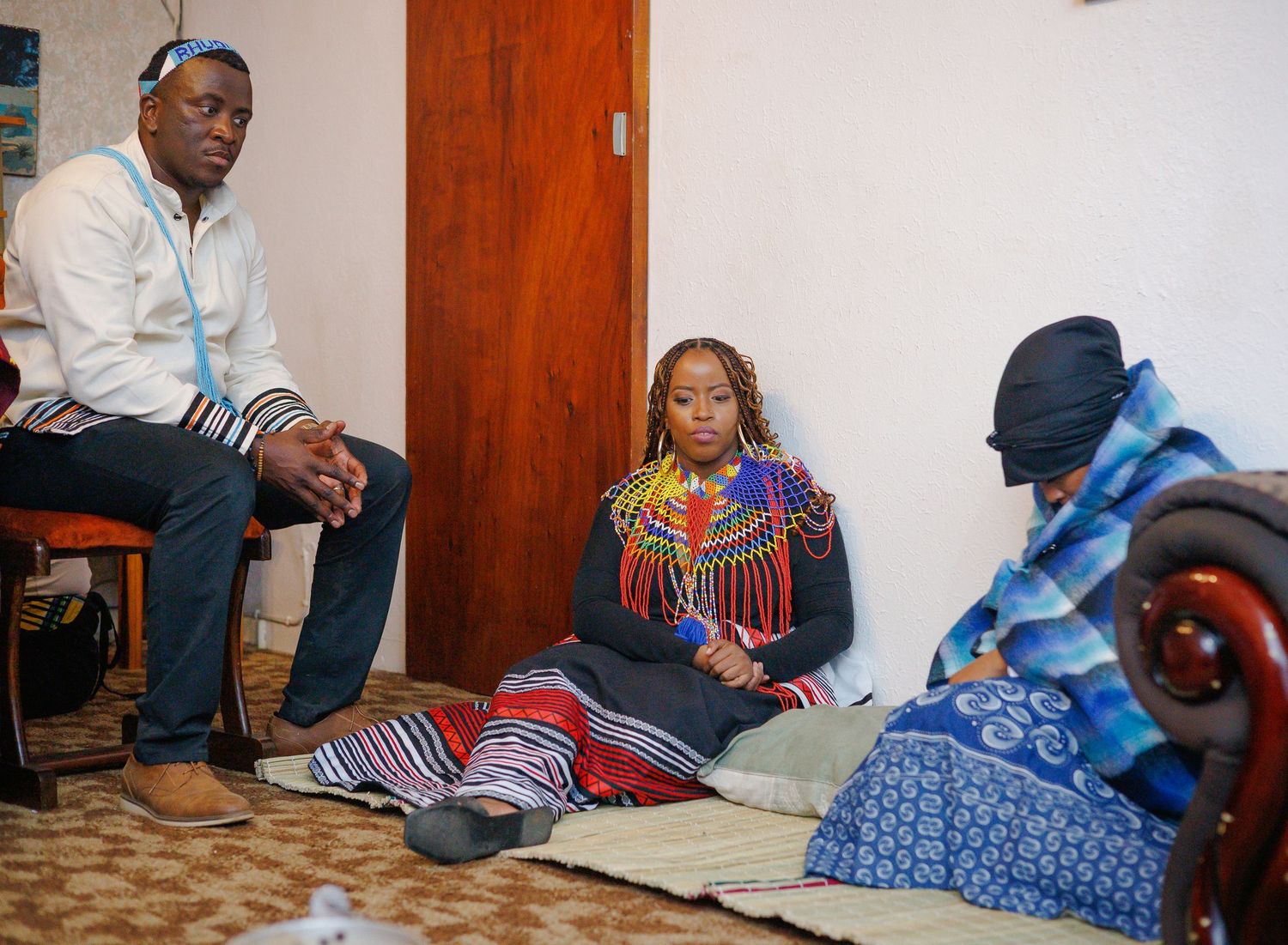Man and woman in traditional Xhosa attire sitting with an elder during a cultural ceremony.
