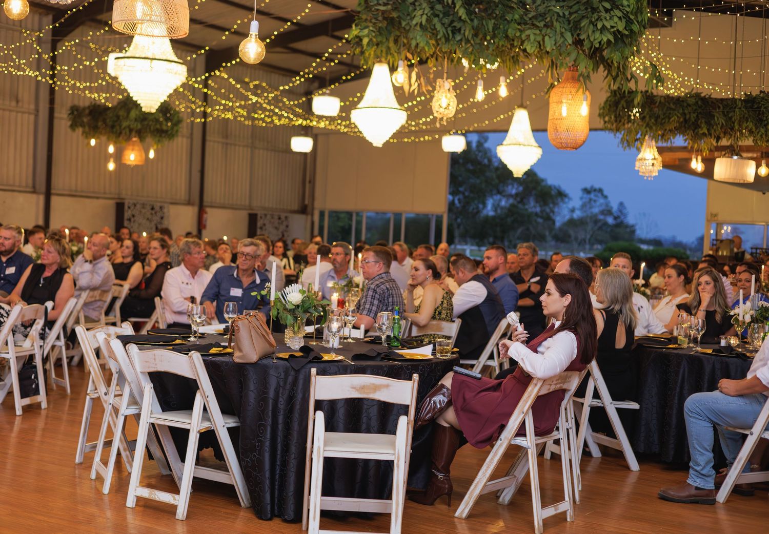 Large group of guests seated at elegantly decorated tables under hanging lights at an indoor event.