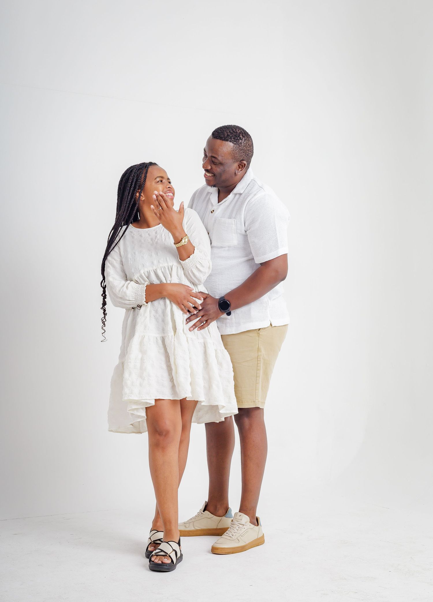 Smiling couple in coordinating white outfits sharing a joyful moment in a bright studio setting.