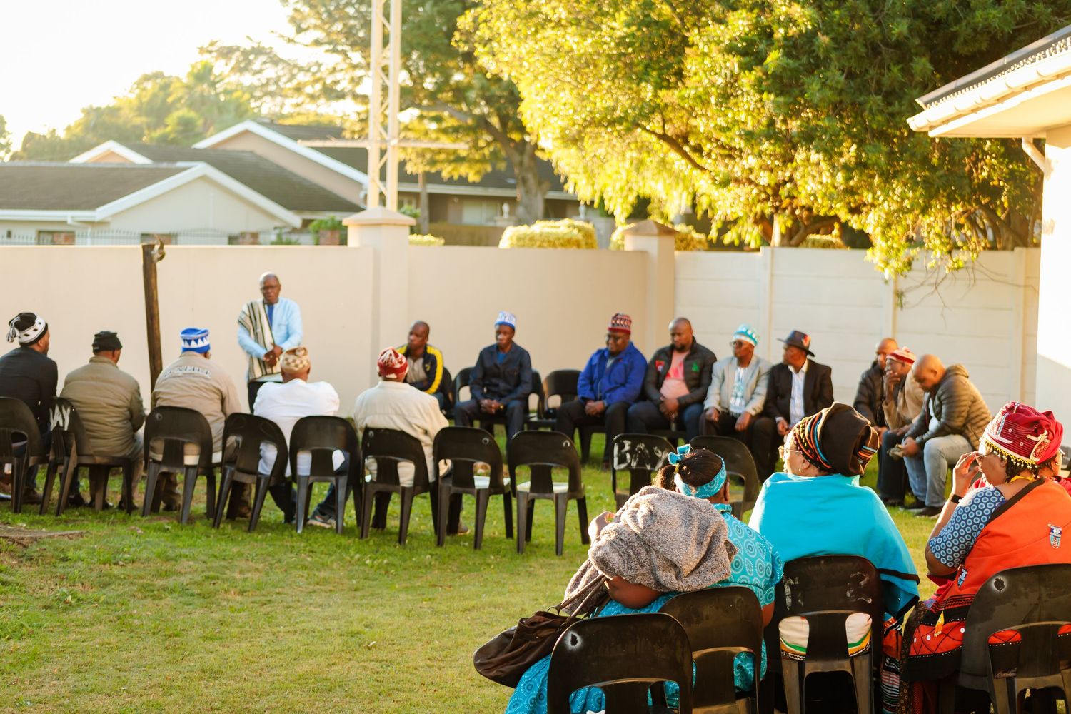 Group of people seated in circle on lawn during traditional African cultural gathering outdoors.