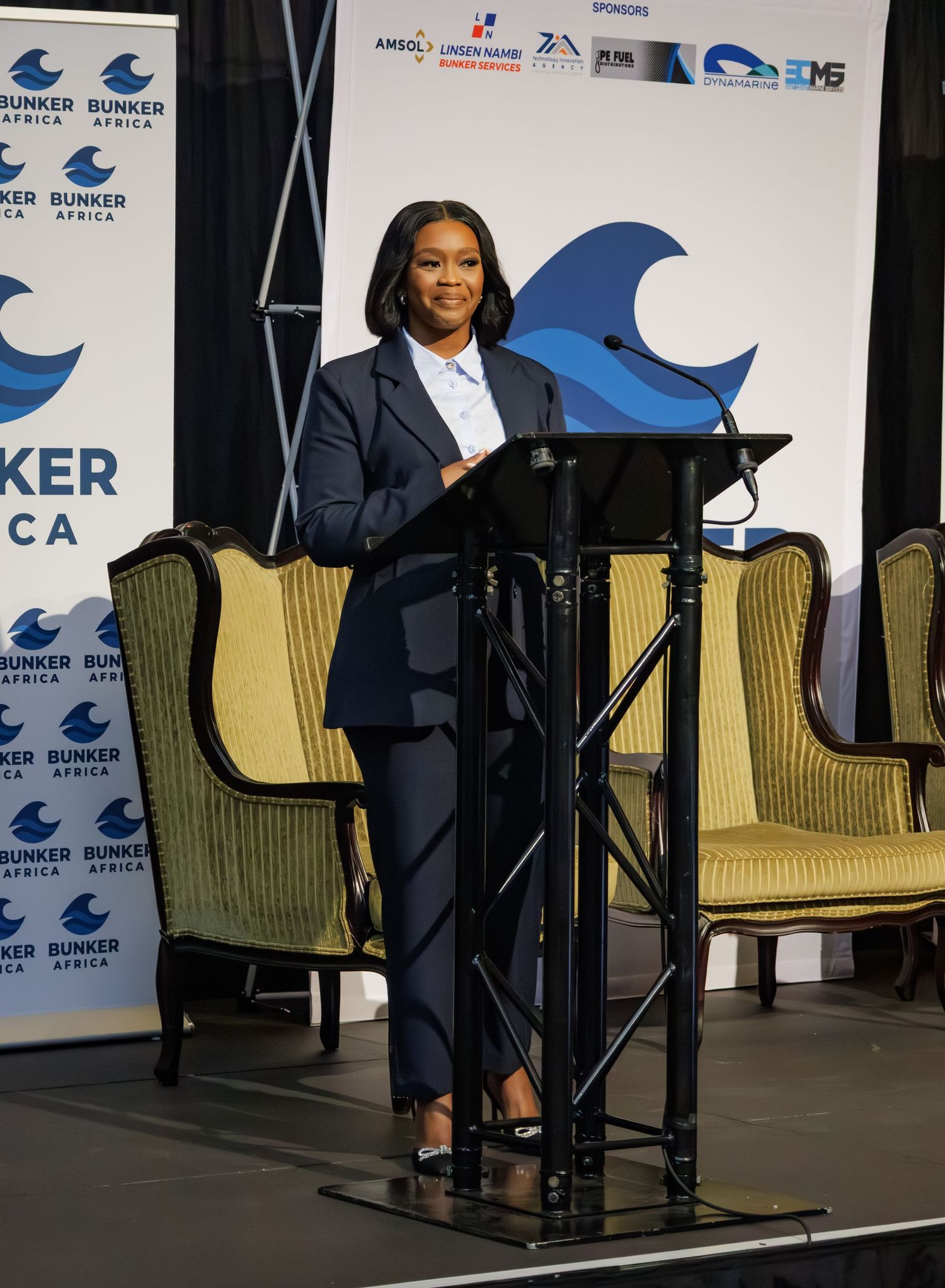 Woman in navy suit delivers speech at podium during Bunker Africa conference event.