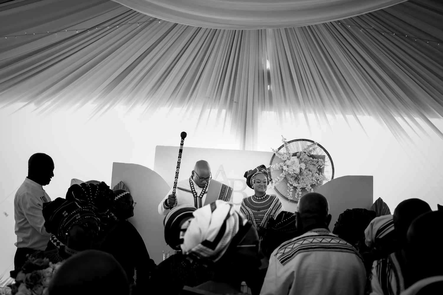 Black and white photo of a traditional African wedding ceremony under a white tent.