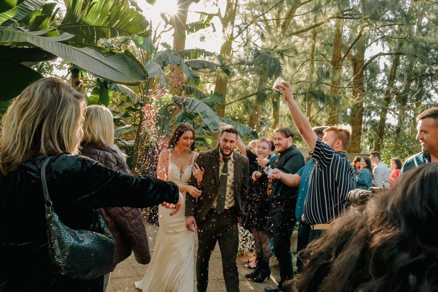 Joyful newlyweds celebrated with confetti by cheering guests during outdoor garden wedding ceremony exit.