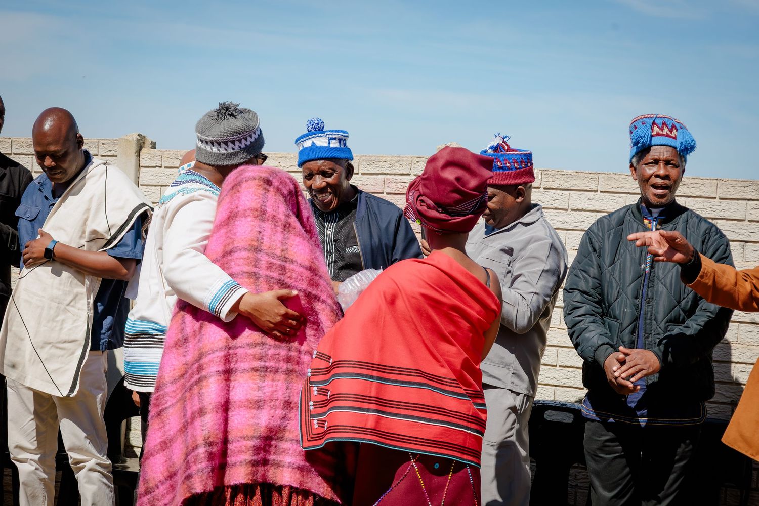 Group of men in traditional Xhosa attire greet each other warmly at an outdoor cultural gathering.