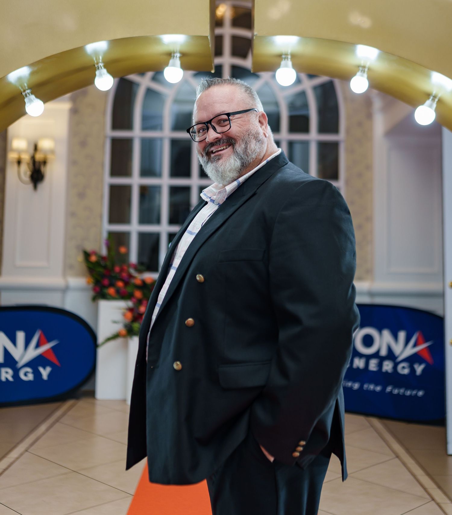 Smiling bearded man in black blazer with gold buttons at a Beyond Energy corporate event.