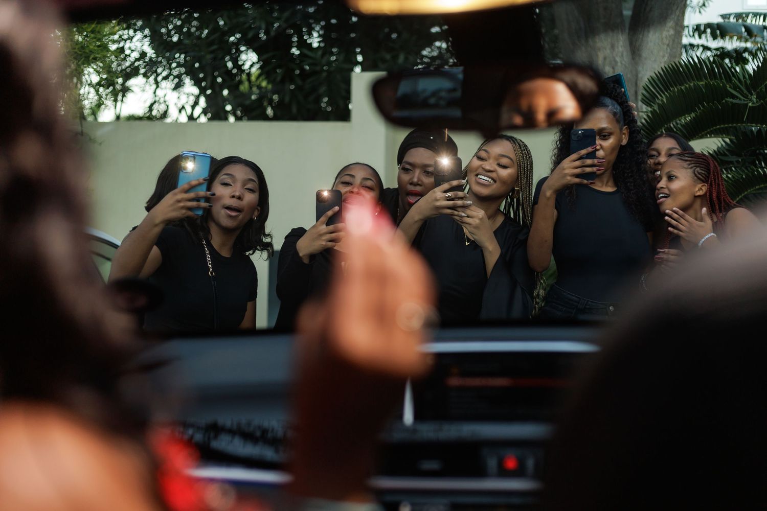 Group of women in black outfits taking selfies with smartphones at an evening outdoor event.