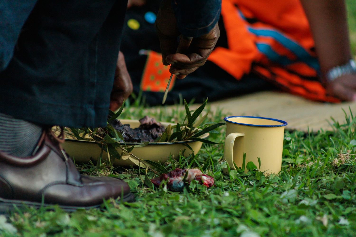 Close-up of hands arranging food in a bowl on grass during a traditional African ceremony.
