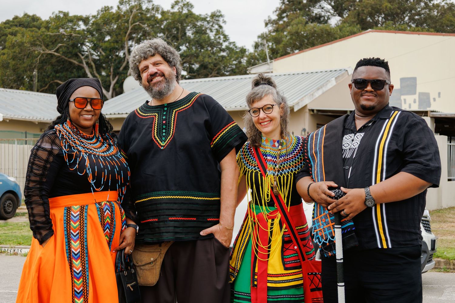 Four people pose together wearing vibrant traditional African attire at a cultural celebration outdoors.