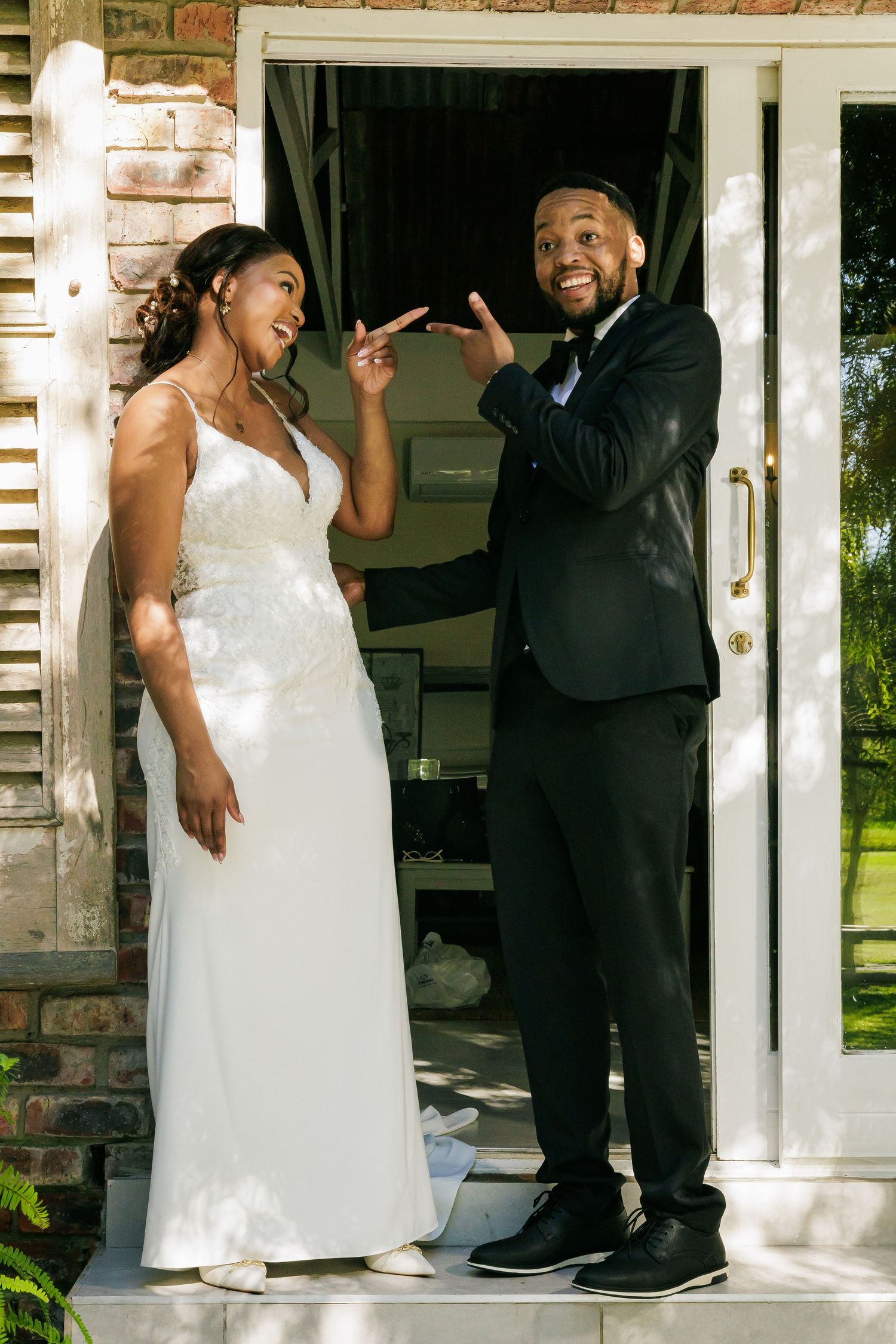 Joyful bride and groom posing playfully together at the entrance of a brick building.