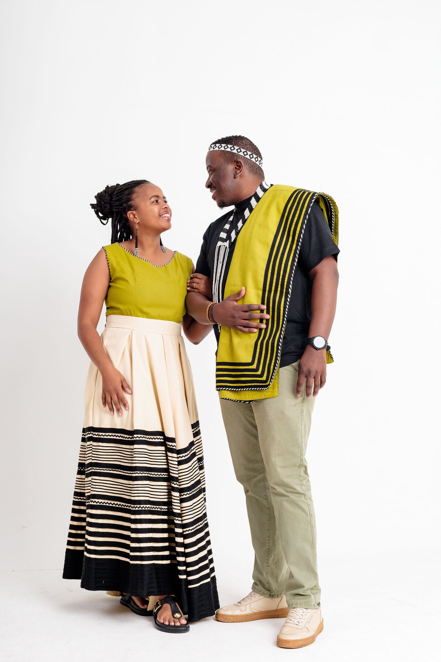 Couple in traditional African Xhosa attire with yellow and black patterns posing in white studio.
