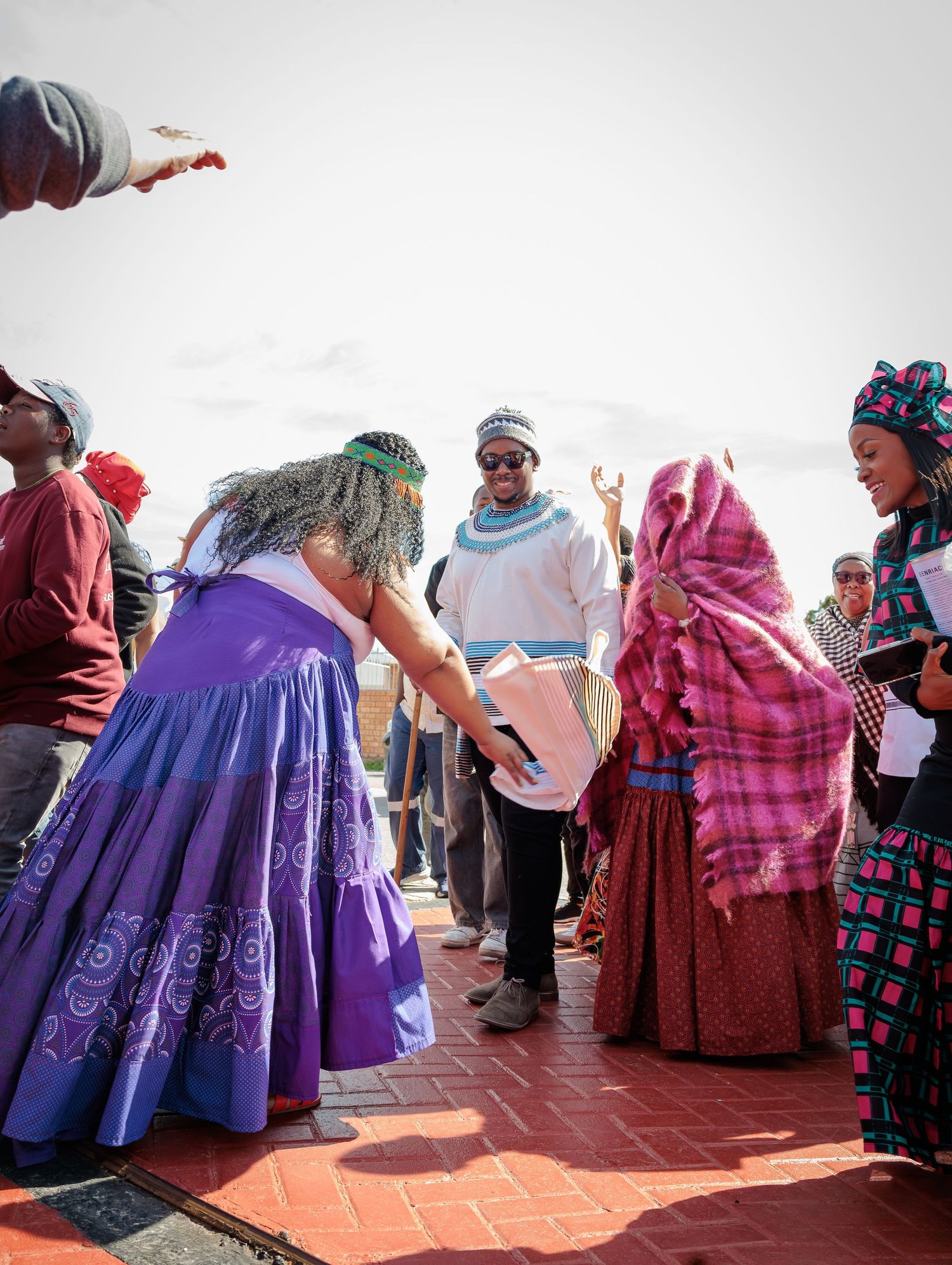A group of people in traditional African attire gather outdoors exchanging gifts during a cultural celebration.