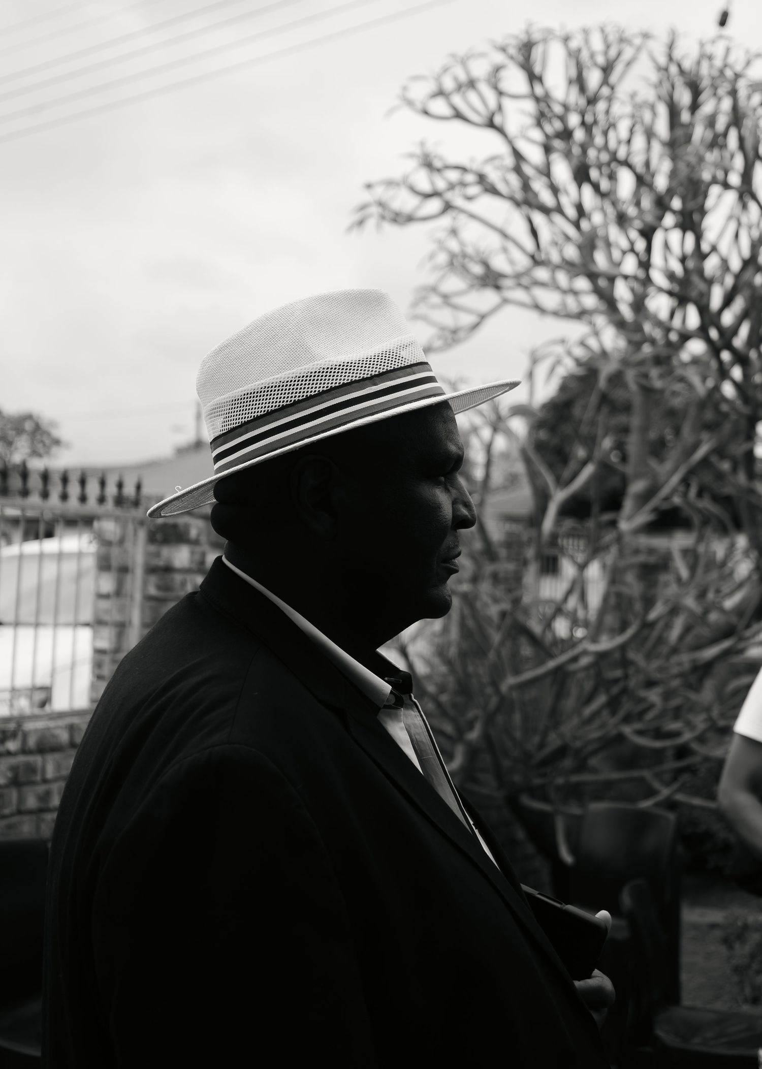 Black and white portrait of a man wearing a stylish hat outdoors with bare trees behind.