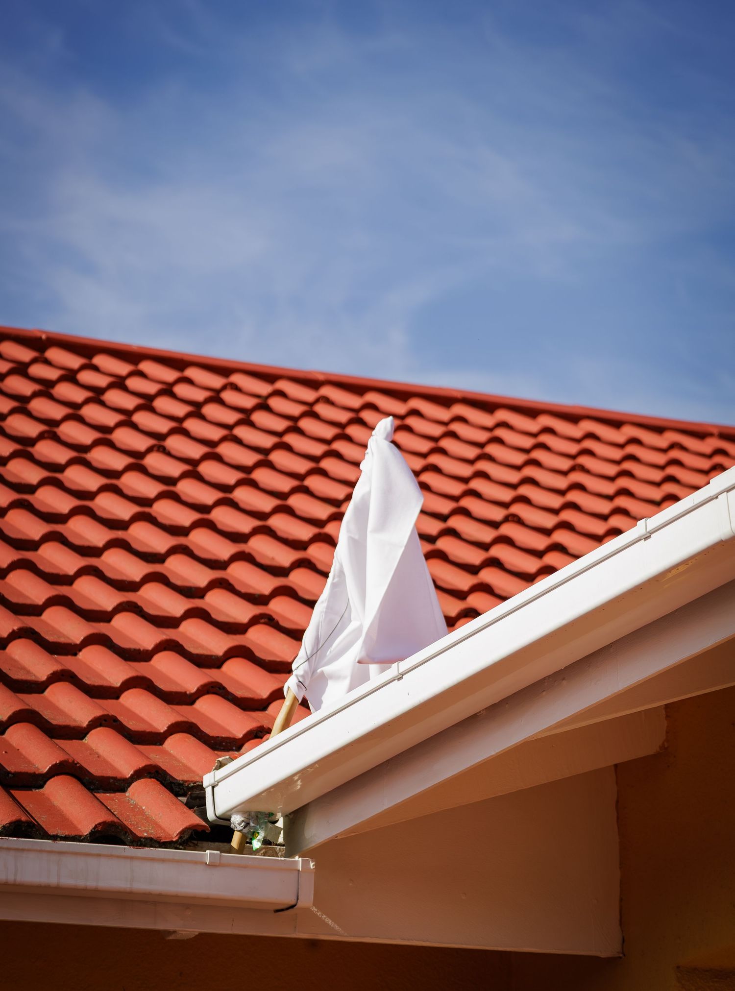 A white fabric flag waves on a red tiled roof against a blue sky with light clouds symbolizing a wedding in Xhosa culture.