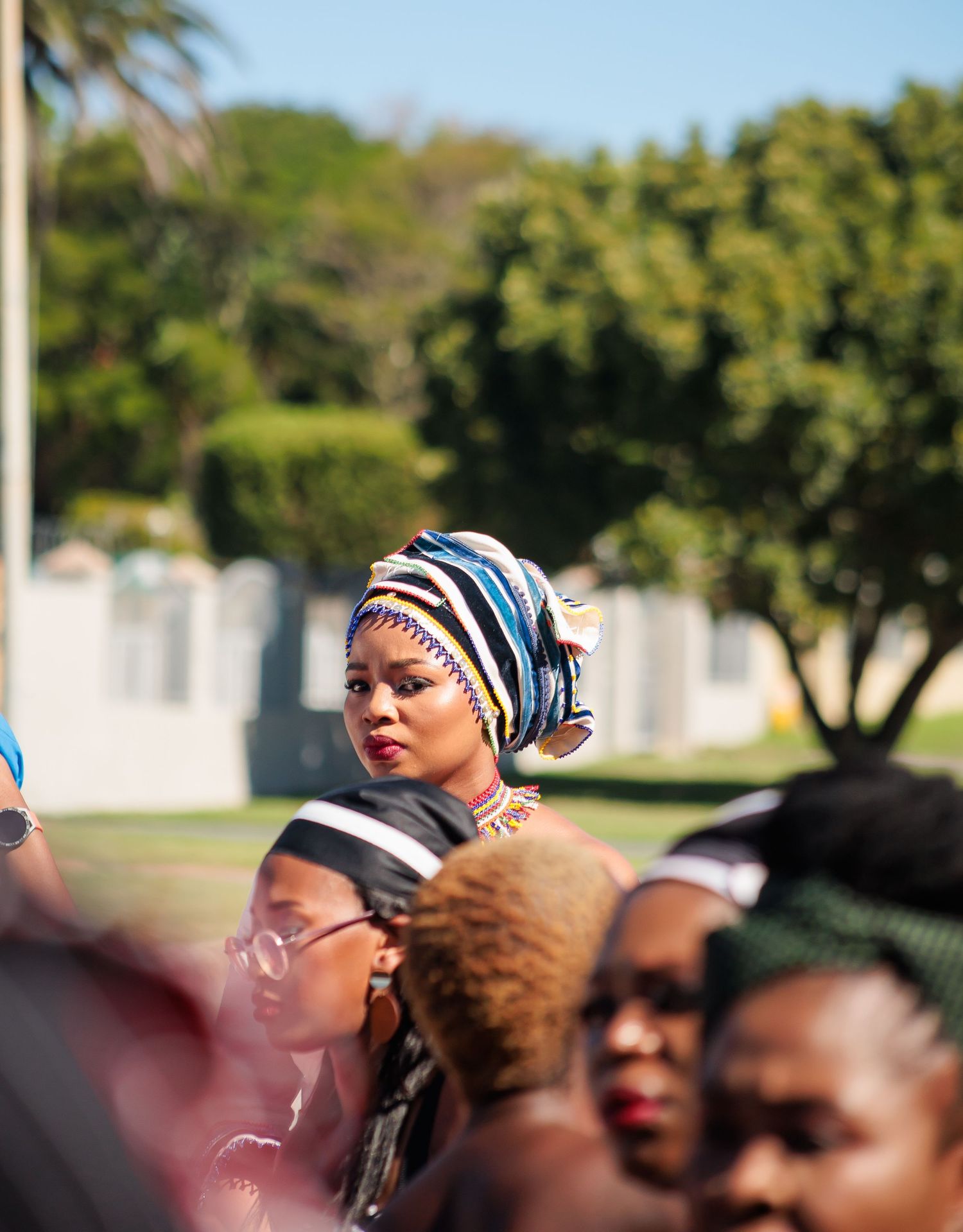 Woman in traditional African head wrap stands out among crowd at outdoor cultural event.