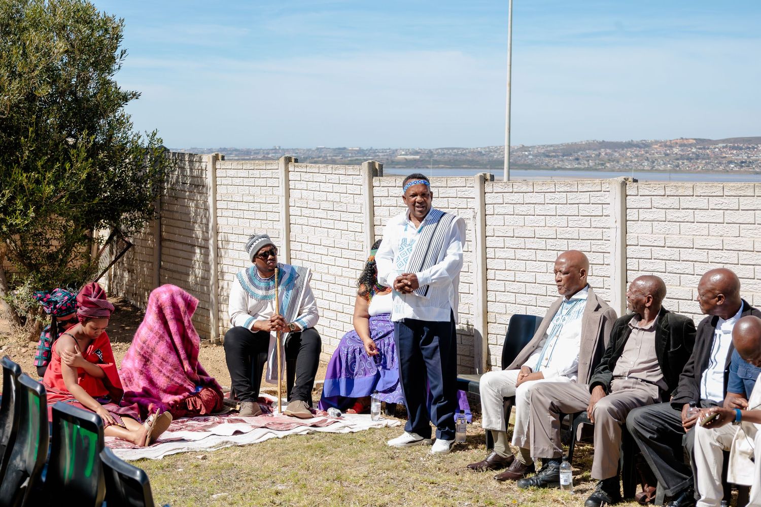 Group of people in traditional African attire gathered outdoors for a formal community meeting.