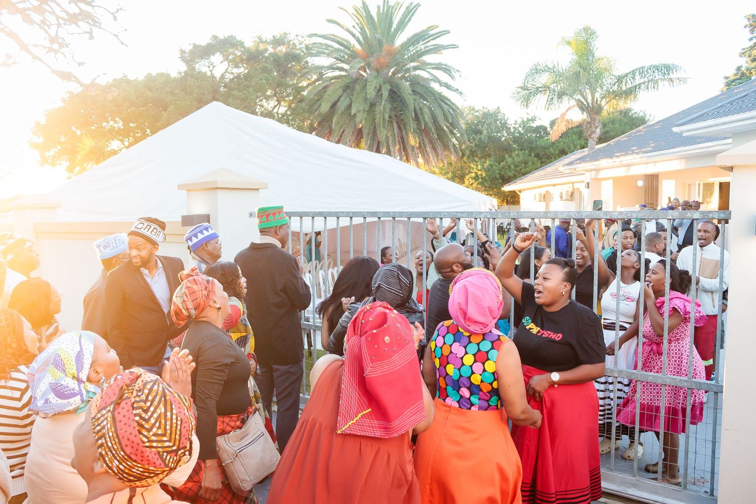 Crowd of guests in colorful traditional attire gathering outside a wedding venue at sunset.