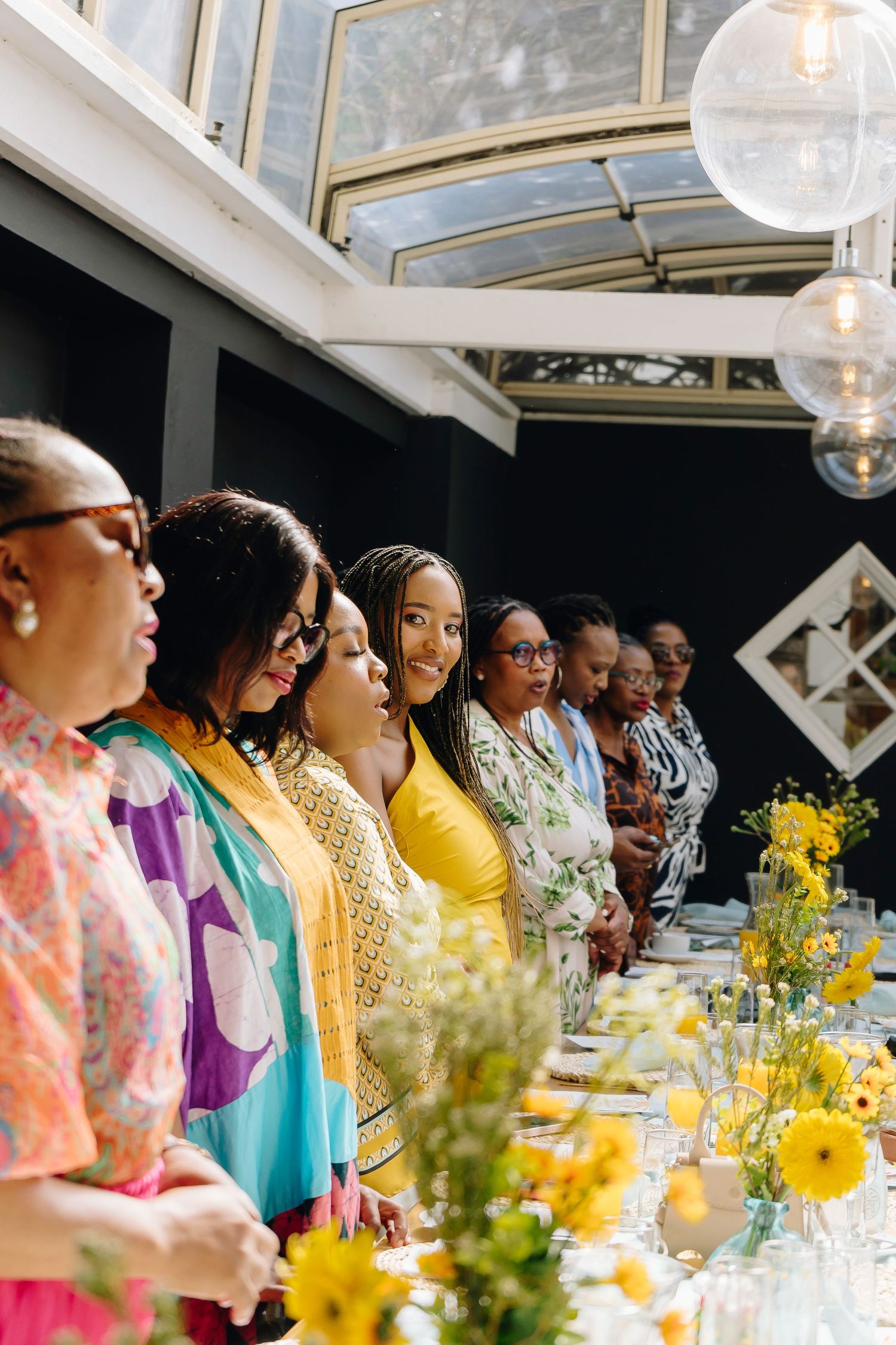Group of women in colorful attire standing beside a decorated table at a celebratory gathering.