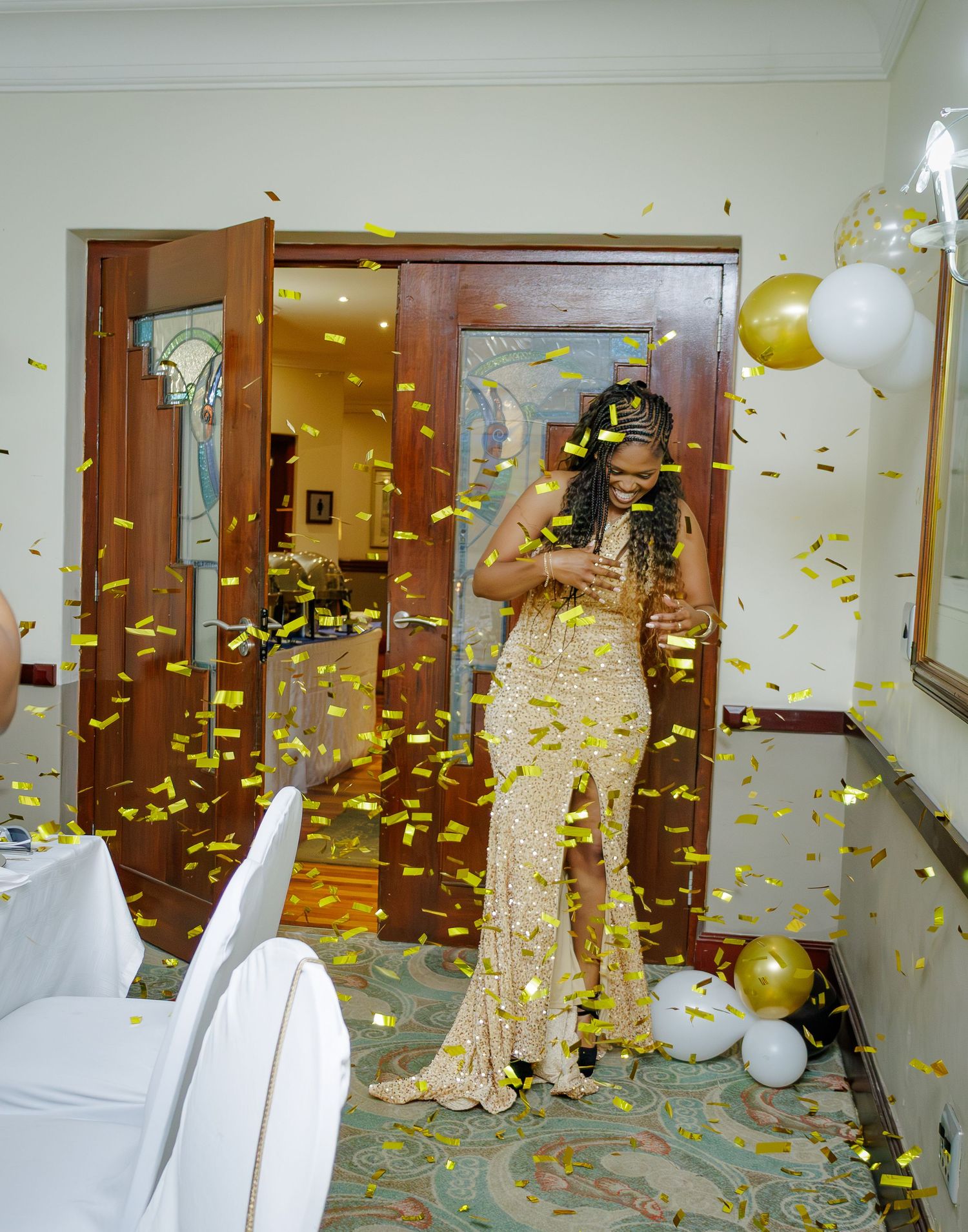 Woman in gold sequin dress covered in falling golden confetti during a glamorous celebration event.